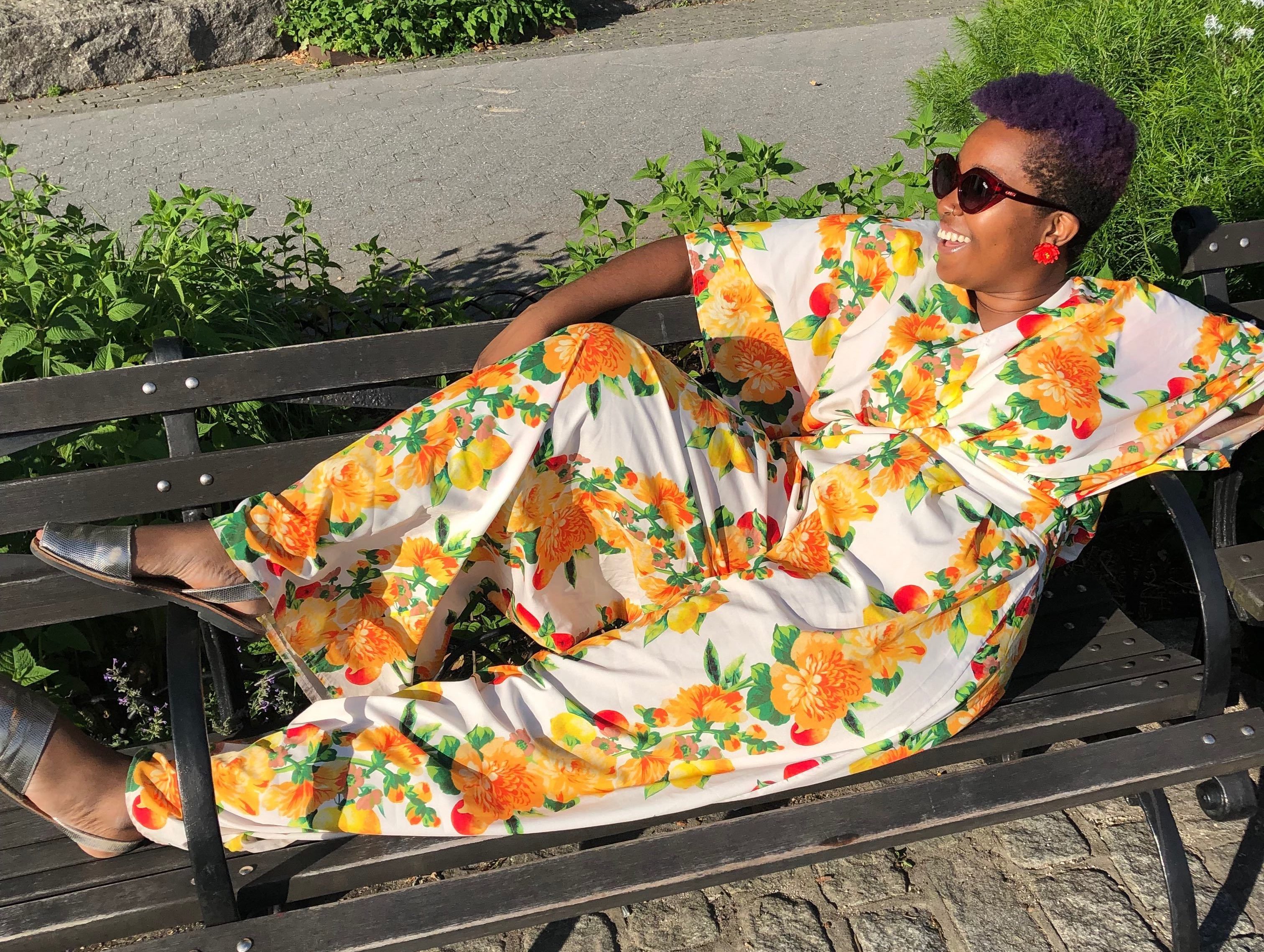 lounging on a bench in Battery Park, wearing a colorful fruit print jumpsuit.